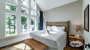 Ein Schlafzimmer mit einem großen Bett, mehreren Fenstern, einer hölzernen Bank und einem Nachttisch mit einer Lampe.