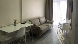 A modern living room with a sofa, a dining table, and chairs. There is a vase with flowers on the table. - D&D Lux Apartment 96. Clean, bright and modern.  (Batumi)