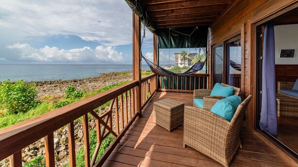 A wooden deck with wicker furniture and a hammock overlooking a rocky coastline. - Port Royal Suite - Ground Level King (West End)