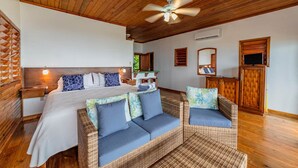 A bedroom with a bed, two wicker sofas, a ceiling fan, and wooden walls. - Port Royal Suite - Ground Level King (West End)