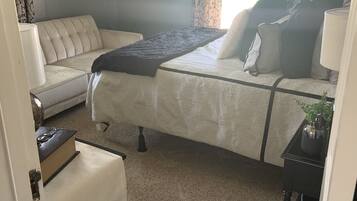 Un dormitorio con cama, sofá, una mesita con lámpara y ventana con cortinas.