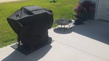 A barbecue grill on a concrete patio with a grassy yard and a house in the background.