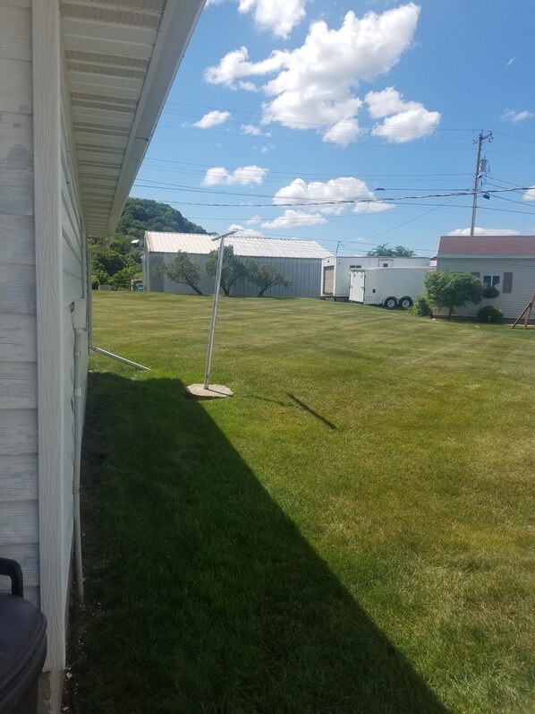 A grassy yard with a white house, a trailer, and a metal pole.