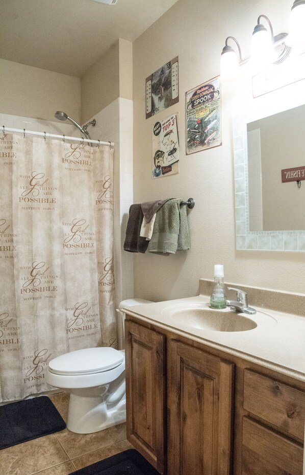 A bathroom with a shower curtain, toilet, sink, and wooden cabinets.