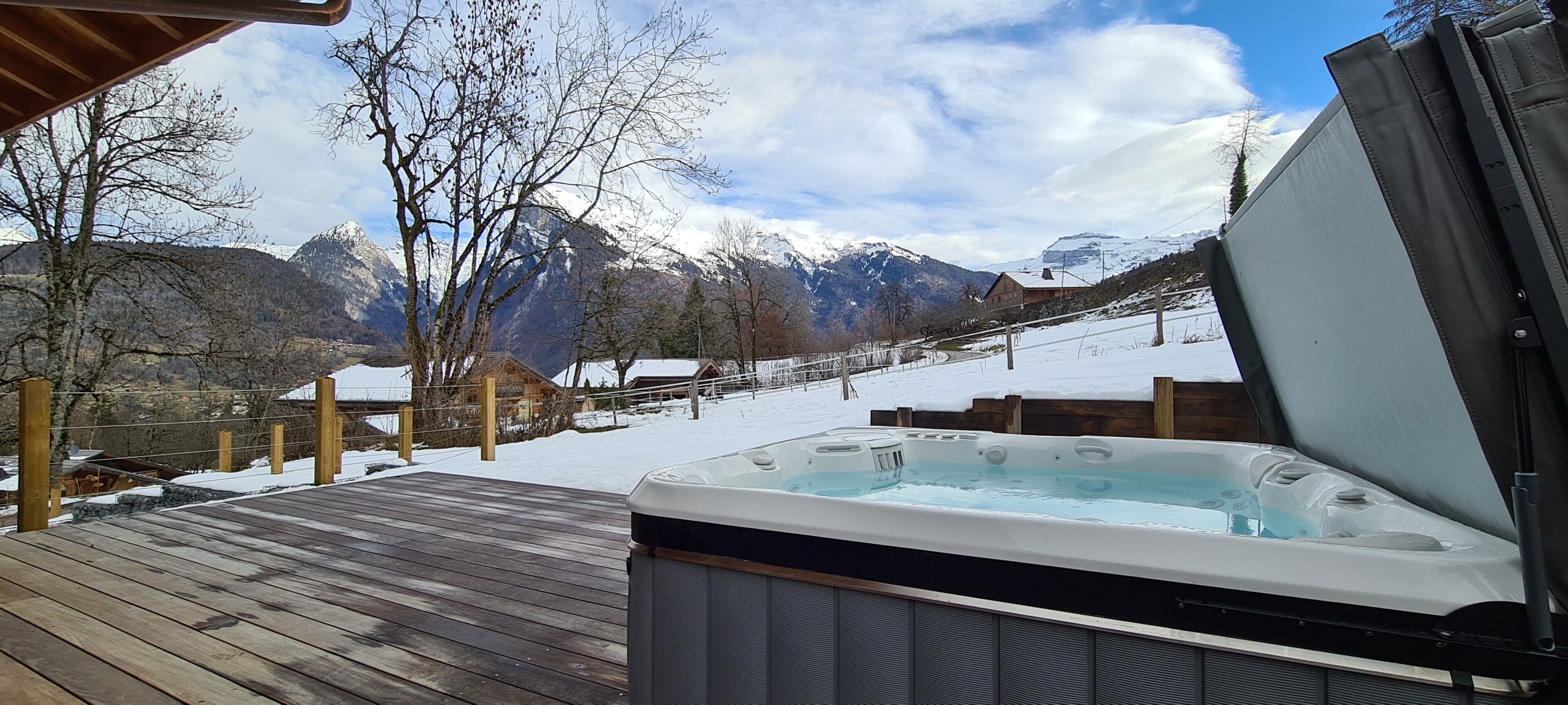 Una terraza de madera con jacuzzi, paisaje nevado y montañas al fondo.