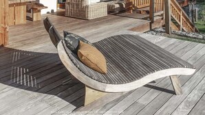 Una terraza de madera con un banco curvo y un conjunto de sofá de mimbre.