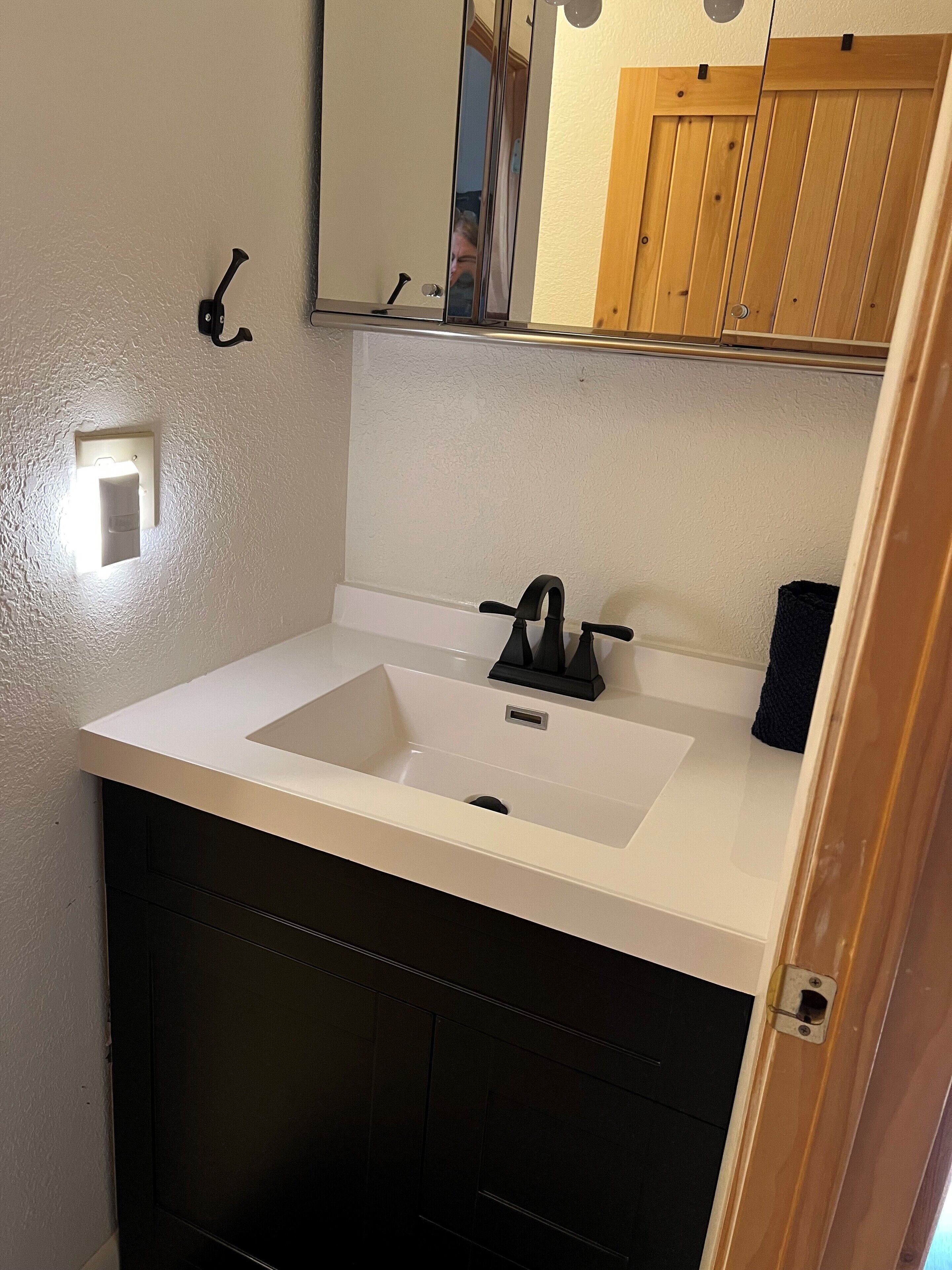 Ein Badezimmer mit einem weißen Waschbecken, einem Spiegel und einem Hängeschrank aus Holz.