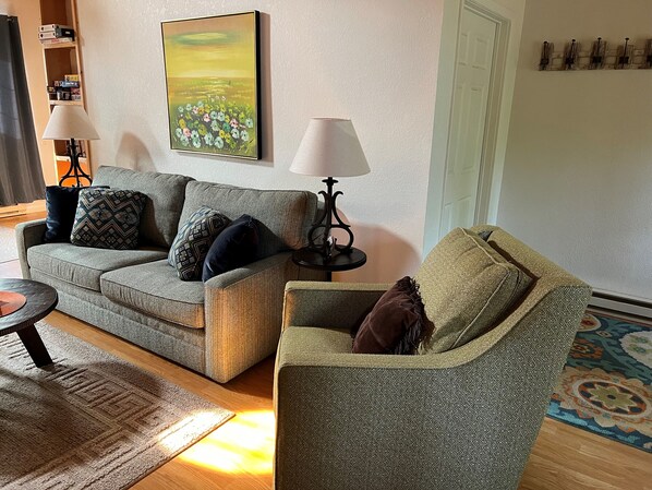A living room with a sofa, a side table, a lamp, a patterned rug, and a painting on the wall.