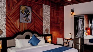 A hotel room with a large bed, a bench, a chair, a wardrobe, and a mirror.