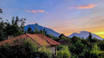 A house with a red-tiled roof, surrounded by lush greenery and mountains in the background.