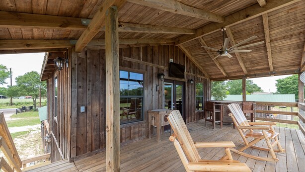 A wooden deck with rocking chairs, a ceiling fan, and a TV mounted on the wall.