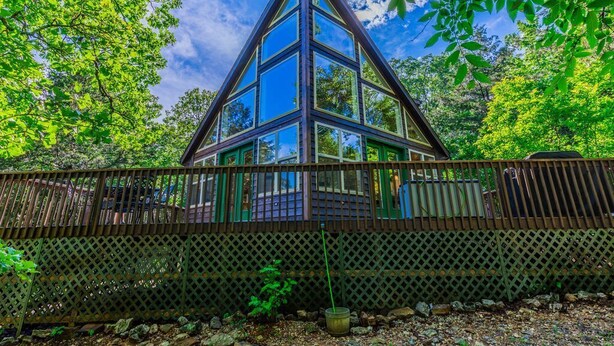 A triangular glass structure surrounded by a wooden fence, set in a forested area.