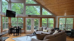 A spacious living area with large windows, a wooden ceiling, and a cozy seating arrangement.