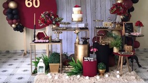 Un espacio decorado para un evento, con un letrero grande que dice '60', un pastel de varios niveles y diversos arreglos florales.