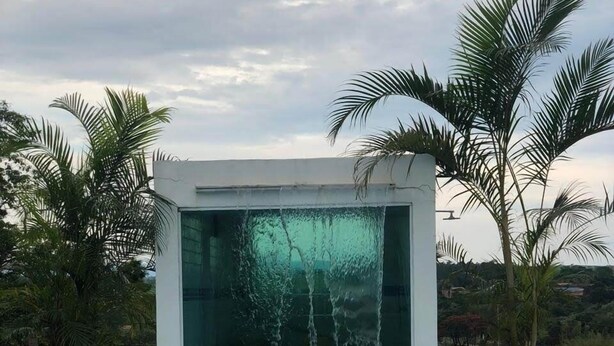 Piscina con caída de agua, rodeada de palmeras y un cielo despejado.