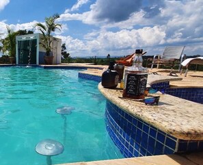 A pool with a water fountain, a bar area with a drink and a menu, and lounge chairs. - Sítio Refúgio do Alto (Piracicaba)