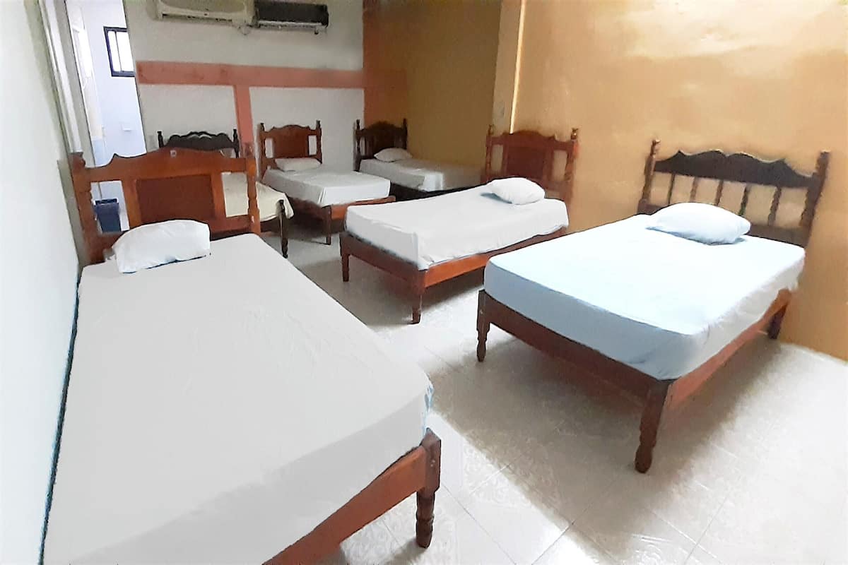 Habitación de hotel con tres camas individuales, cabecera de madera, una mesita y aire acondicionado instalado en la pared.