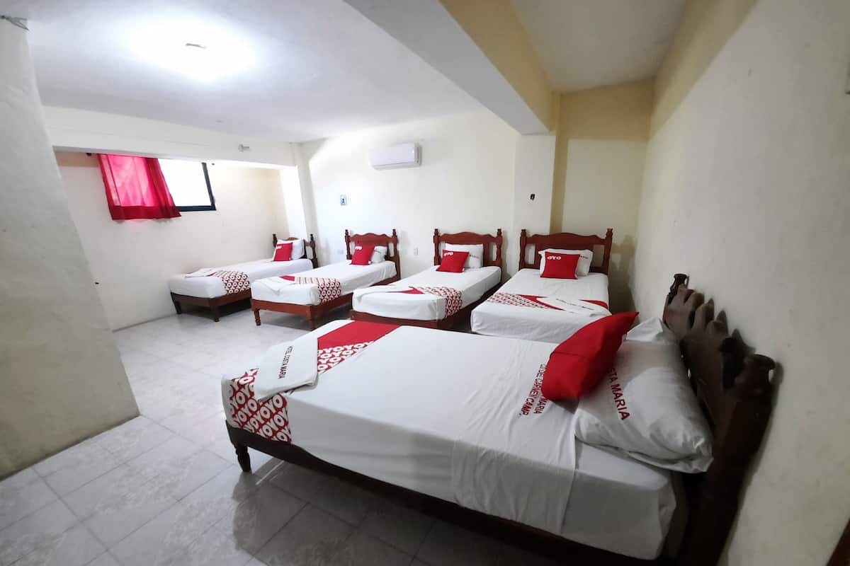 Habitación de hotel con cuatro camas, cada una con ropa blanca y detalles rojos.
