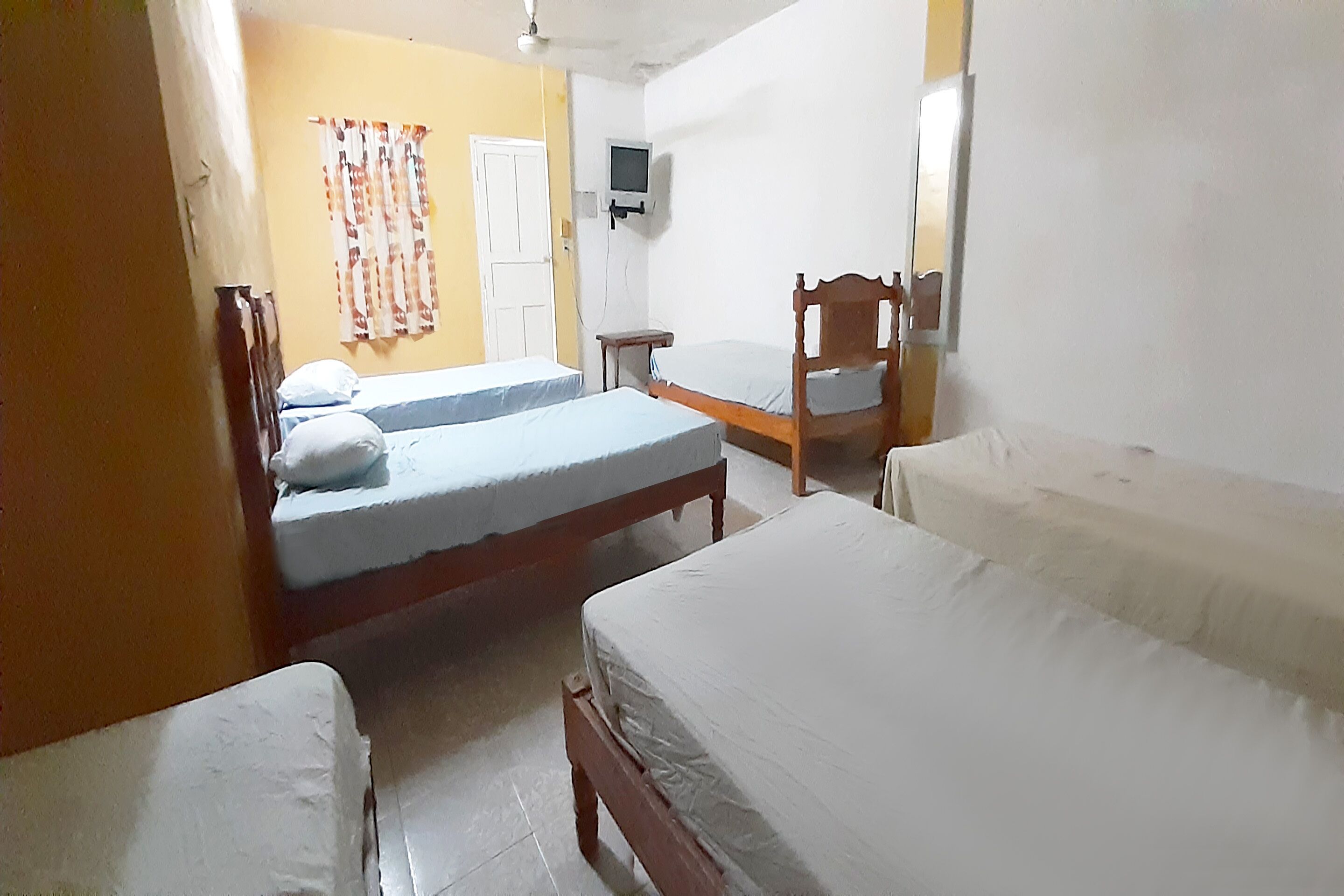 A room with two beds, a small table, and a television on the wall.