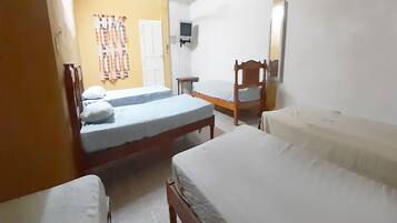 A room with two beds, a small table, and a television on the wall.