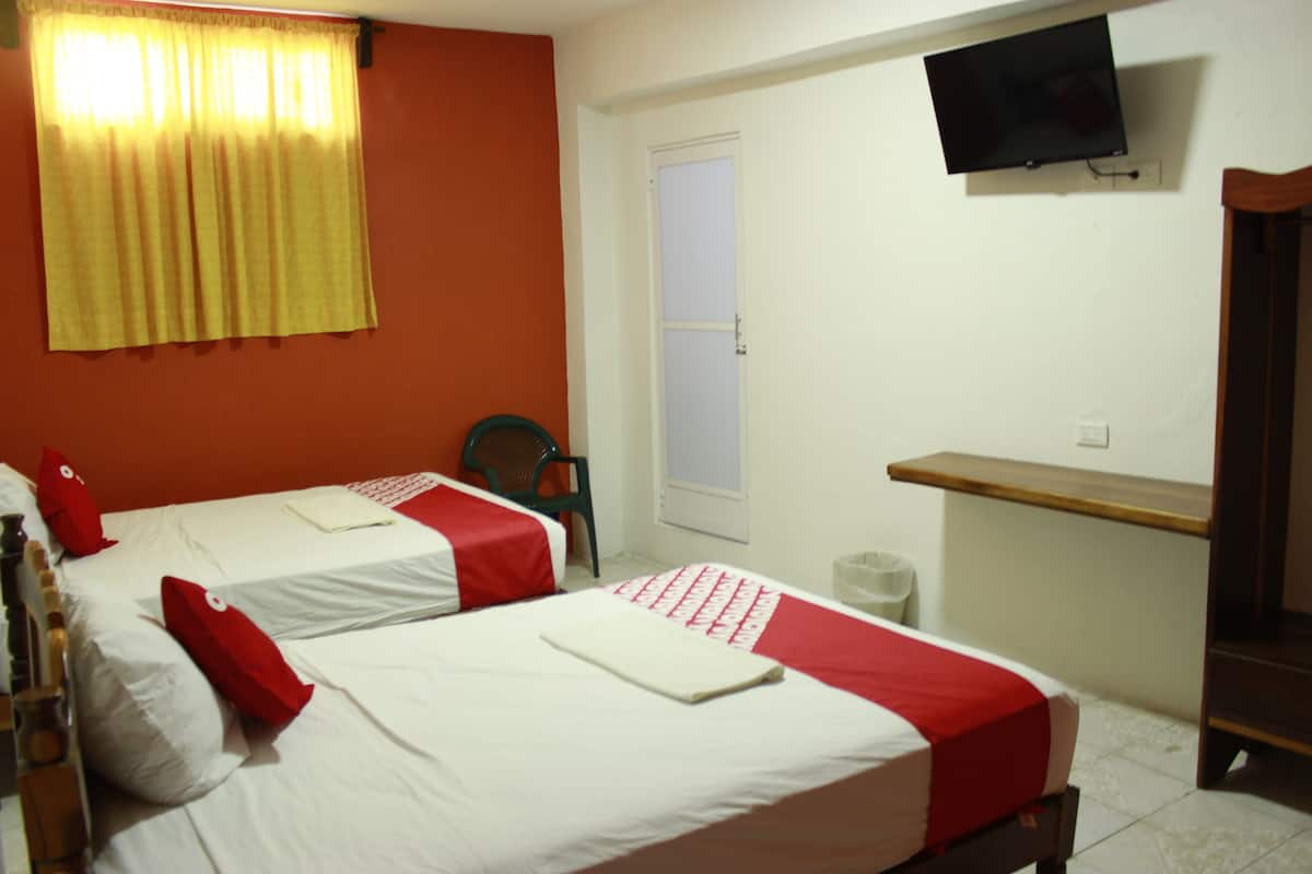 Habitación de hotel con dos camas, un televisor montado en la pared y un estante de madera.