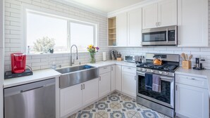 Une cuisine moderne avec des meubles blancs, des appareils en acier inoxydable et un sol carrelé à motifs.
