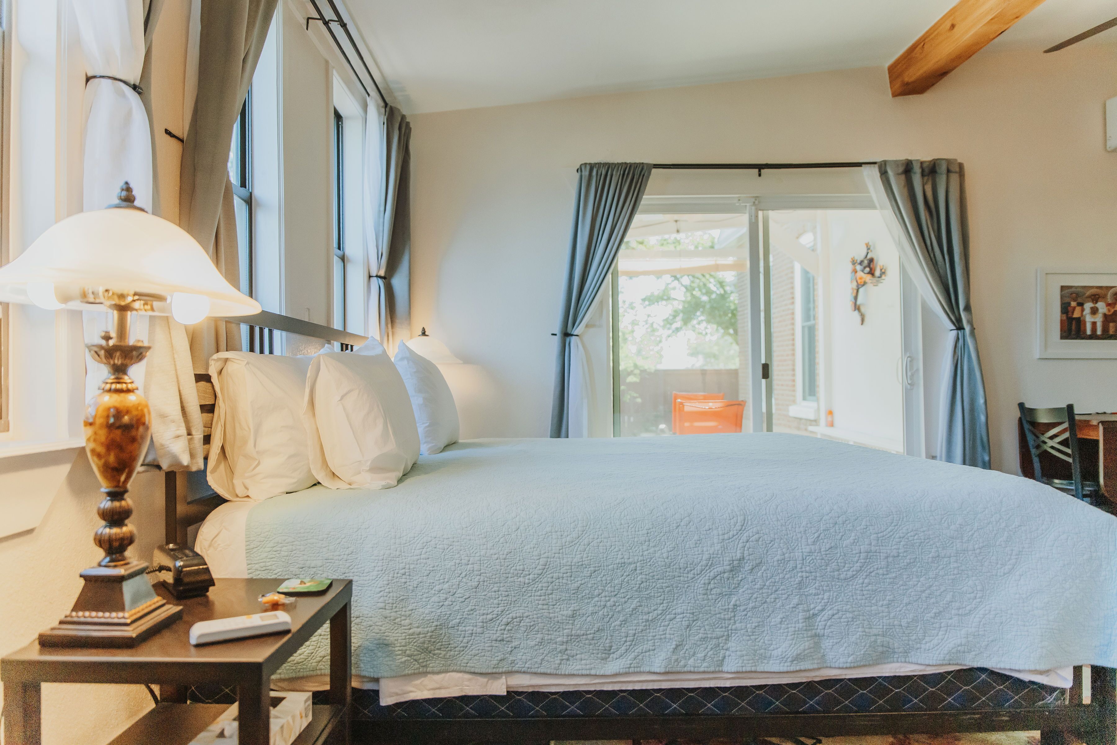 Een slaapkamer met een groot bed, een nachtkastje met een lamp en een raam met gordijnen.