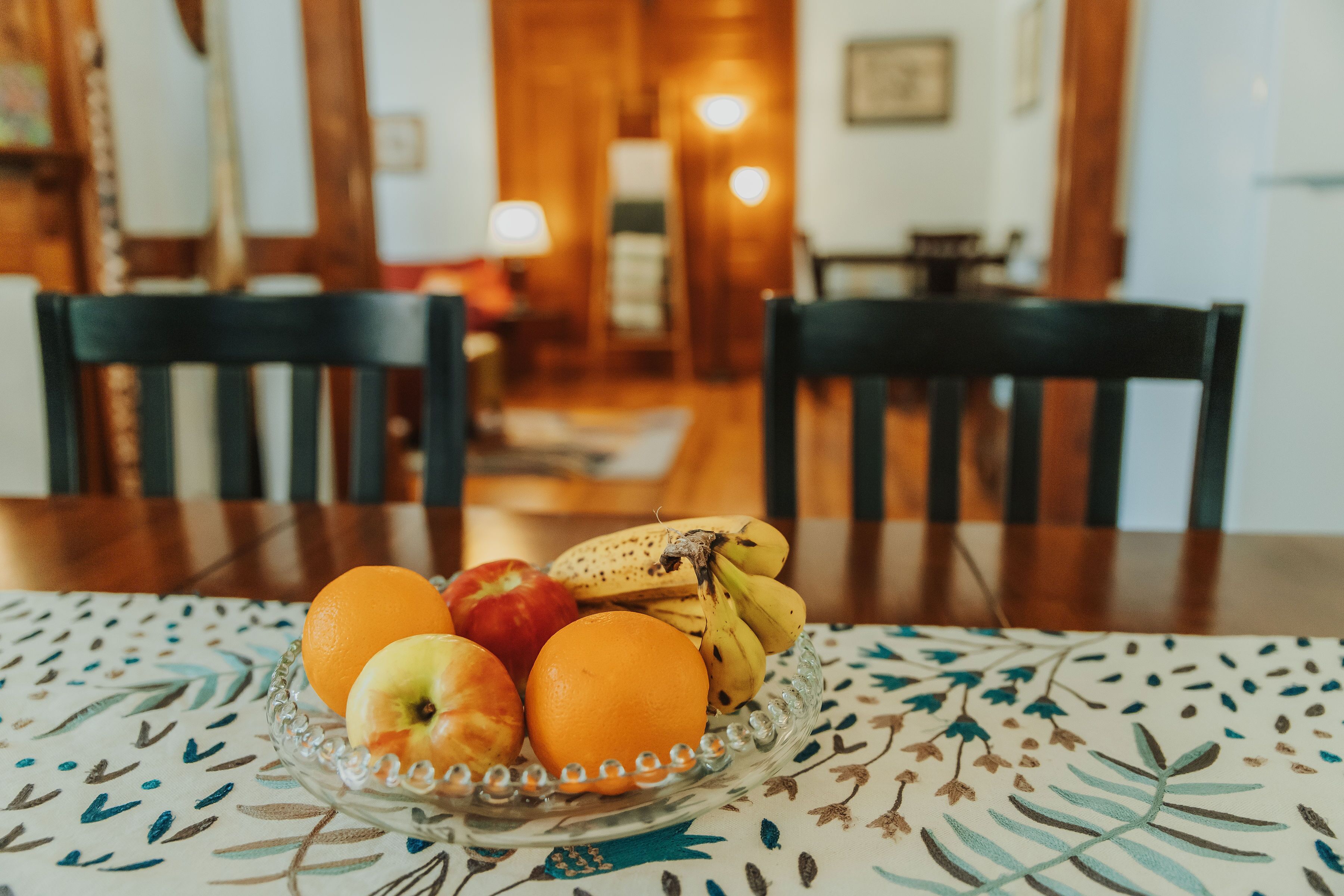 Une table à manger sur laquelle se trouve un panier de fruits contenant des pommes, des oranges et des bananes.