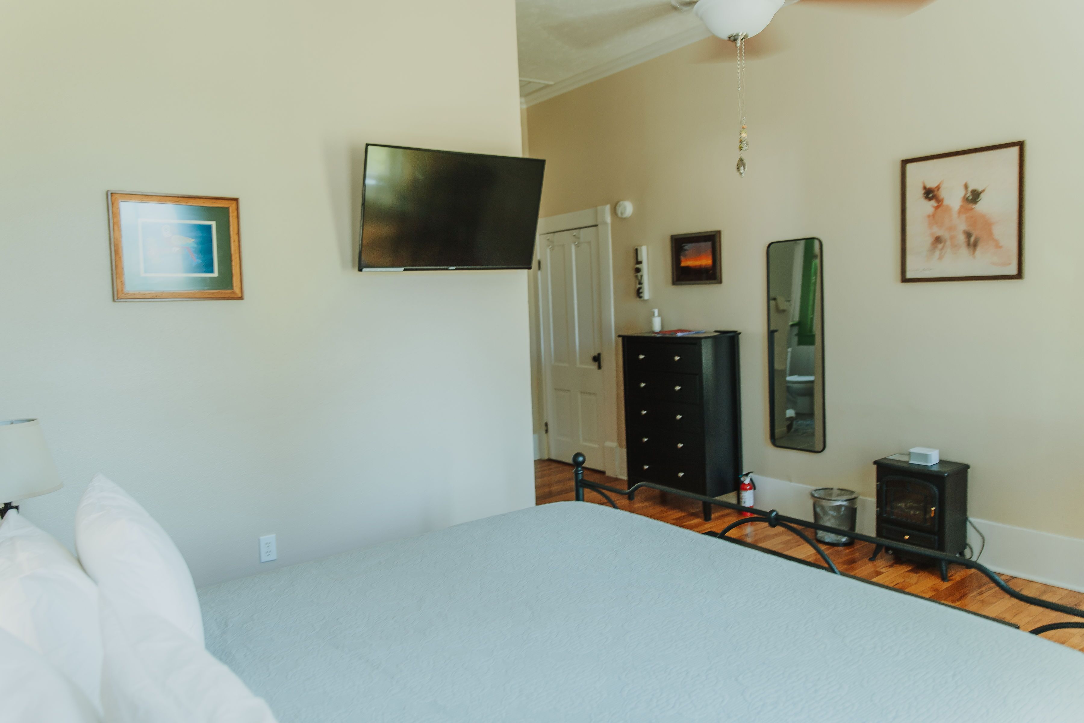 Un dormitorio con cama, televisor, cómoda, espejo y chimenea.