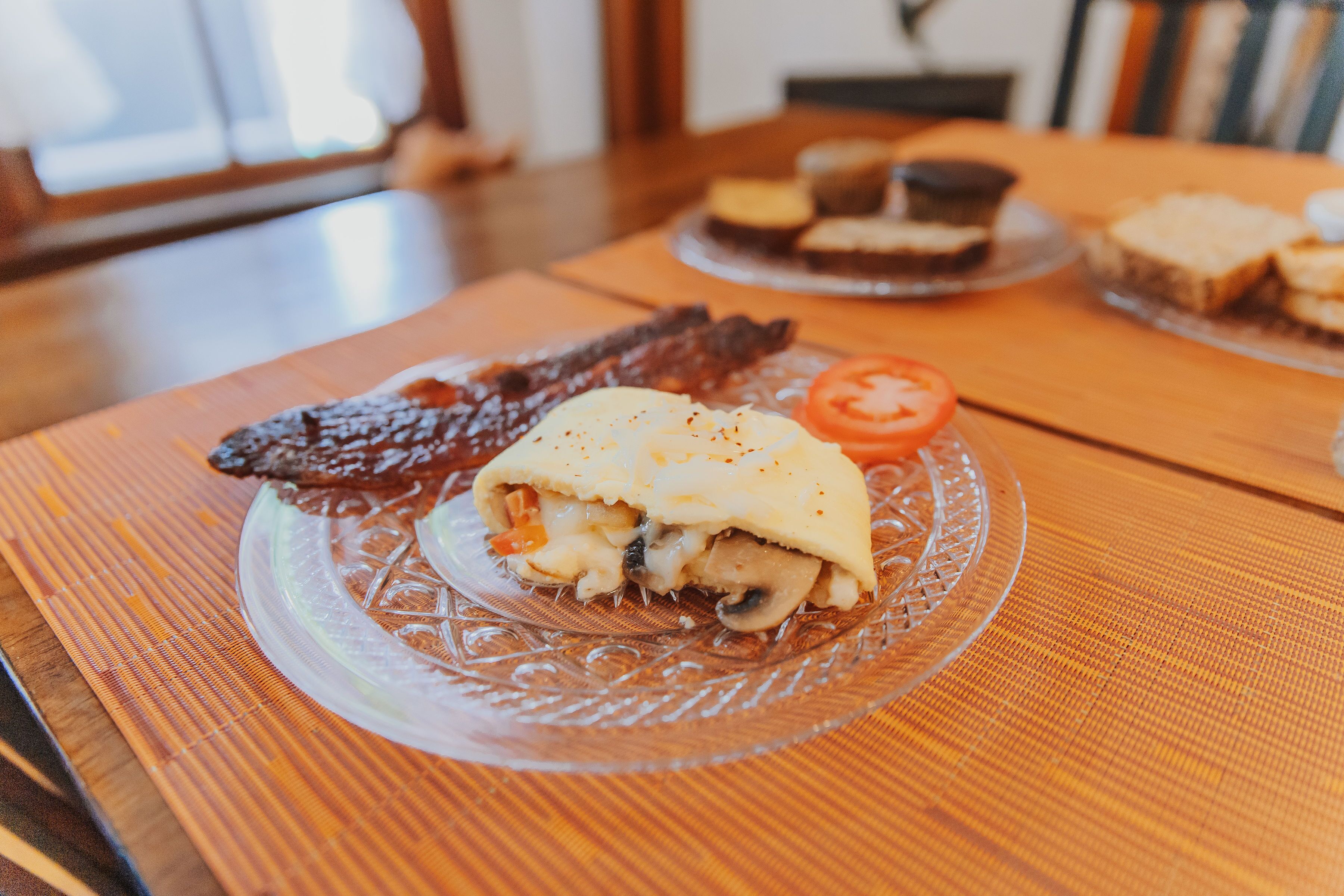 A meal on a glass plate with a slice of tomato and a piece of meat, placed on a wooden table.