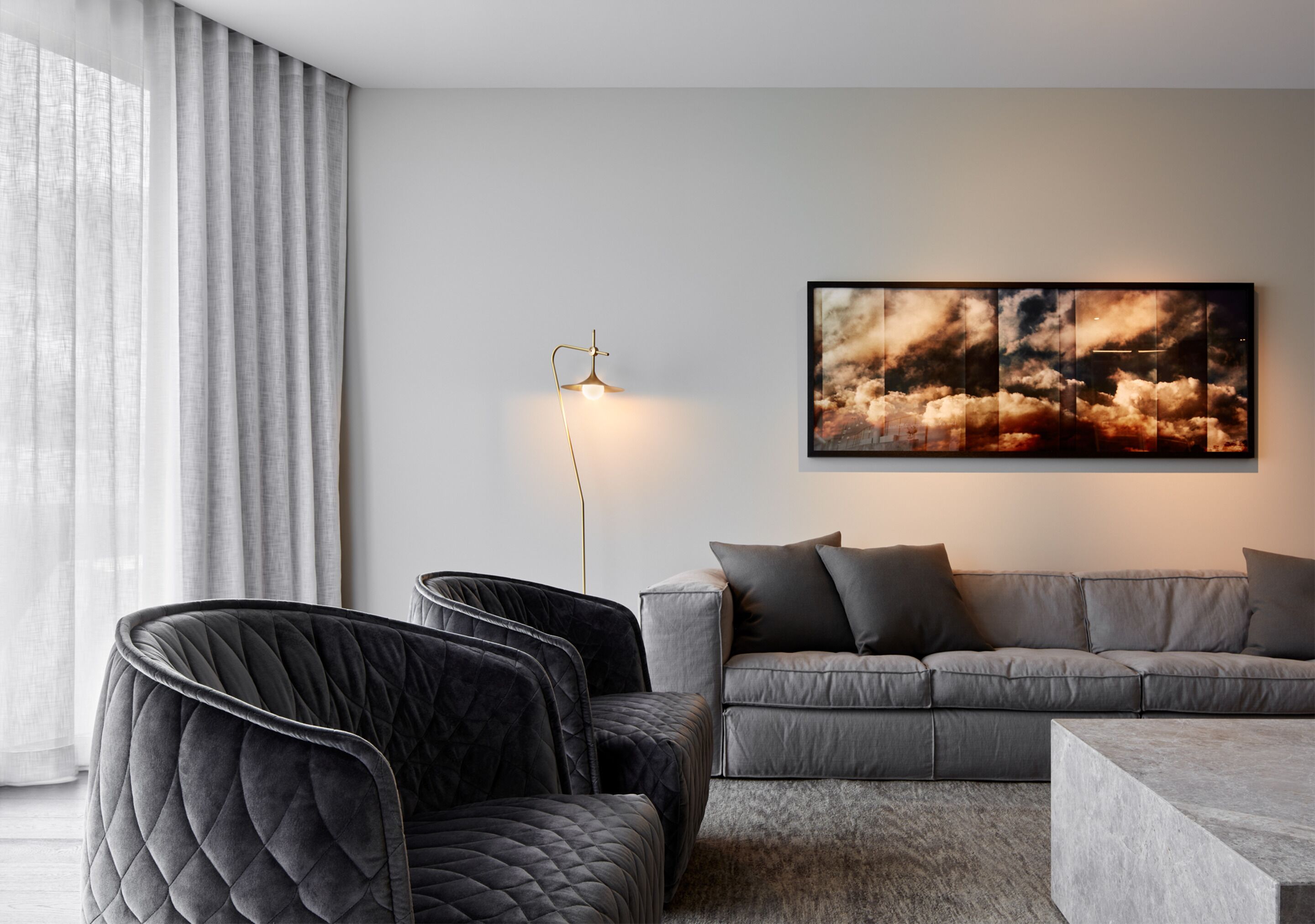 A modern living room with a grey sofa, black armchairs, a floor lamp, and a large abstract painting on the wall.