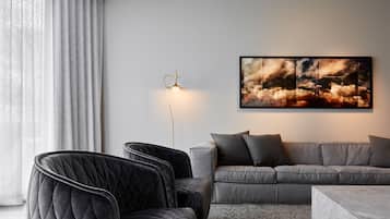 A modern living room with a grey sofa, black armchairs, a floor lamp, and a large abstract painting on the wall.