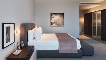 A modern hotel room with a large bed, a bedside table with a glass, and a framed picture on the wall.