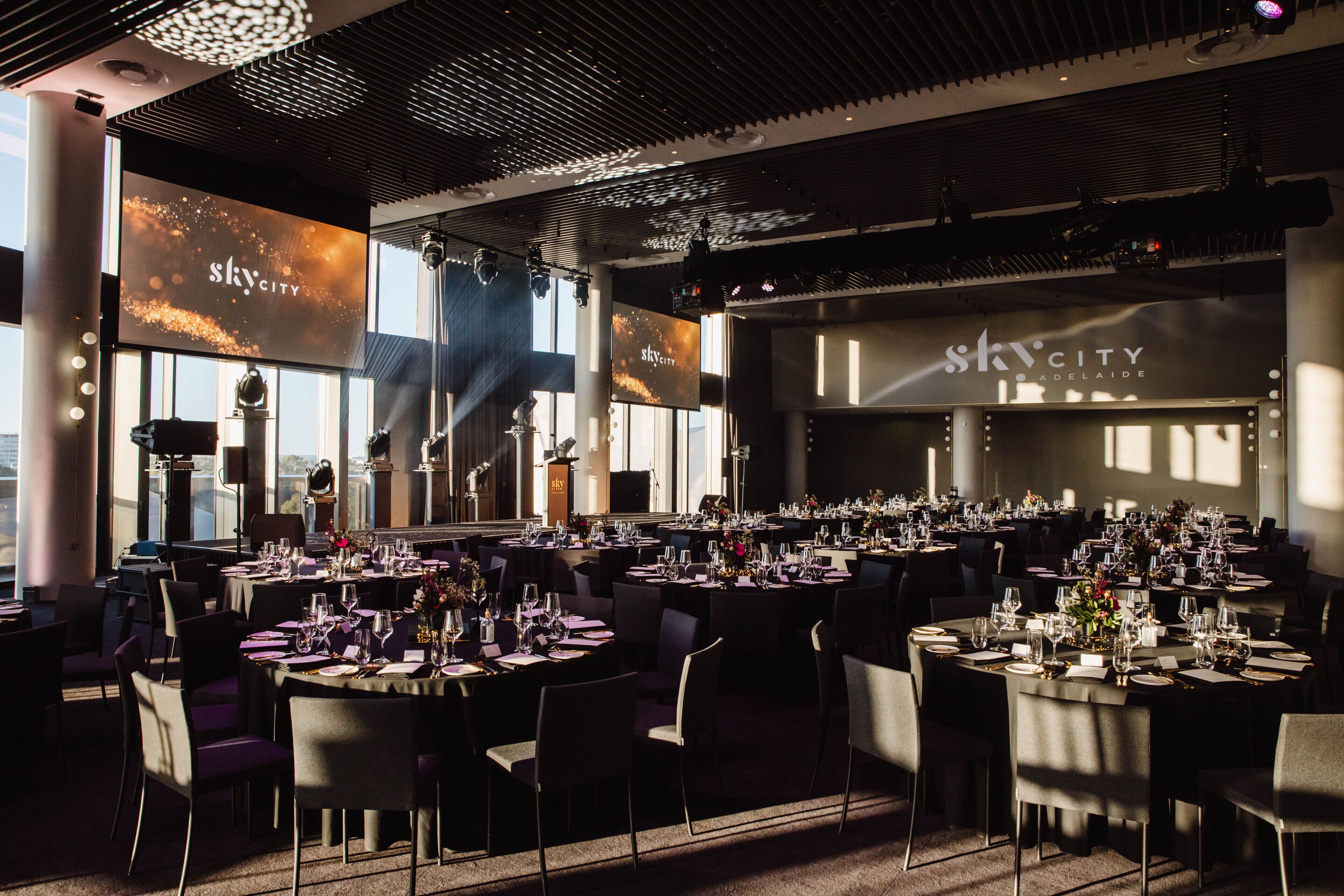 Ett rymligt konferensrum med flera bord uppställda för evenemang, stora fönster och en tydlig skylt med texten ”SkyCity Adelaide”.