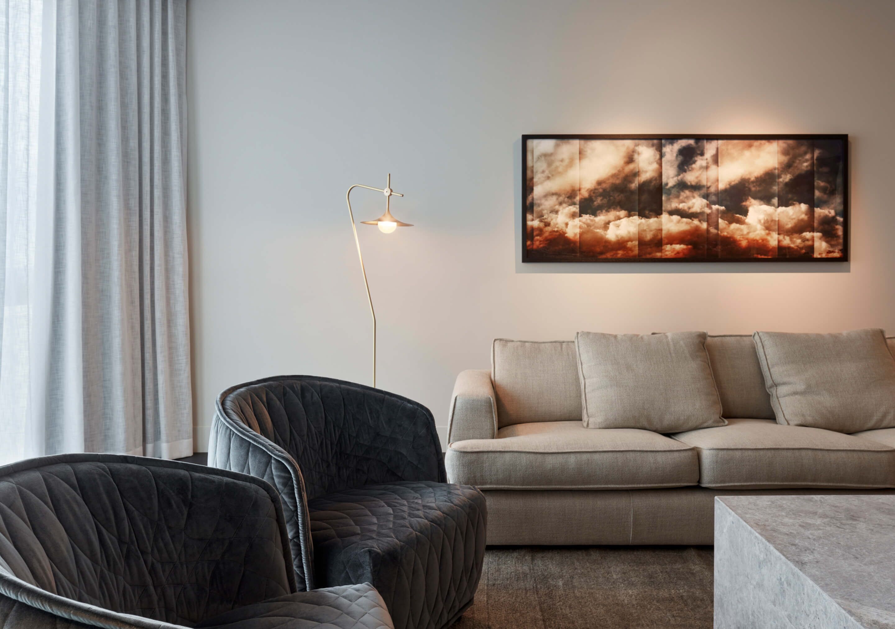 Un salon moderne avec un canapé, deux fauteuils, une lampe sur pied et un grand tableau abstrait accroché au mur.
