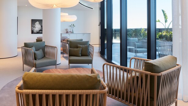Ein modernes Interieur mit Korbmöbeln, großen Fenstern und Blick ins Freie.