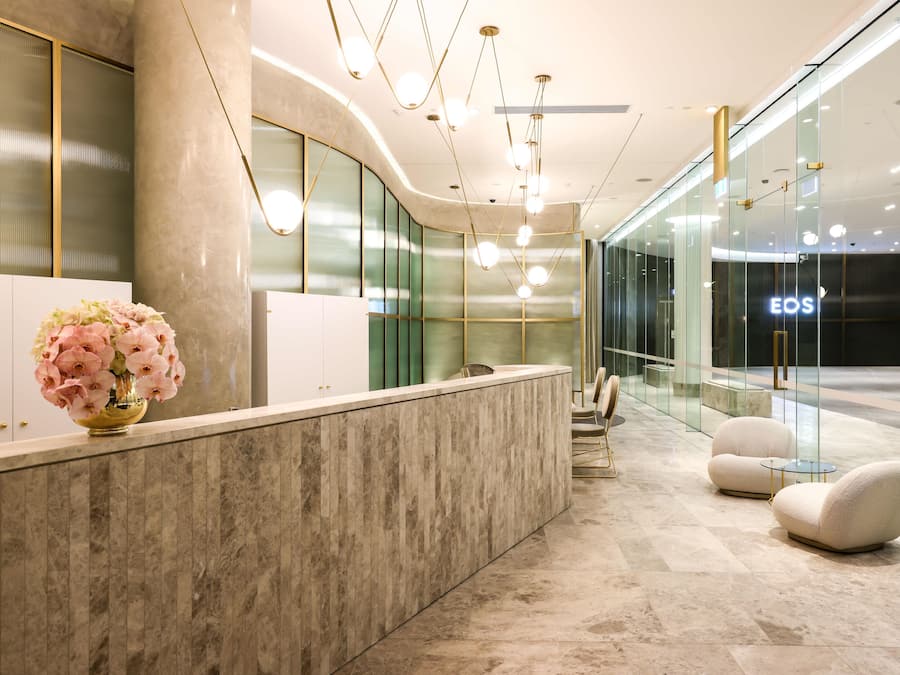 A modern reception area with a marble counter, a vase of pink flowers, and a glass wall with the word "EOS" on it.