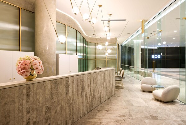 A modern reception area with a marble counter, a vase of pink flowers, and a glass wall with the word "EOS" on it. - Eos by SkyCity (Adelaide)