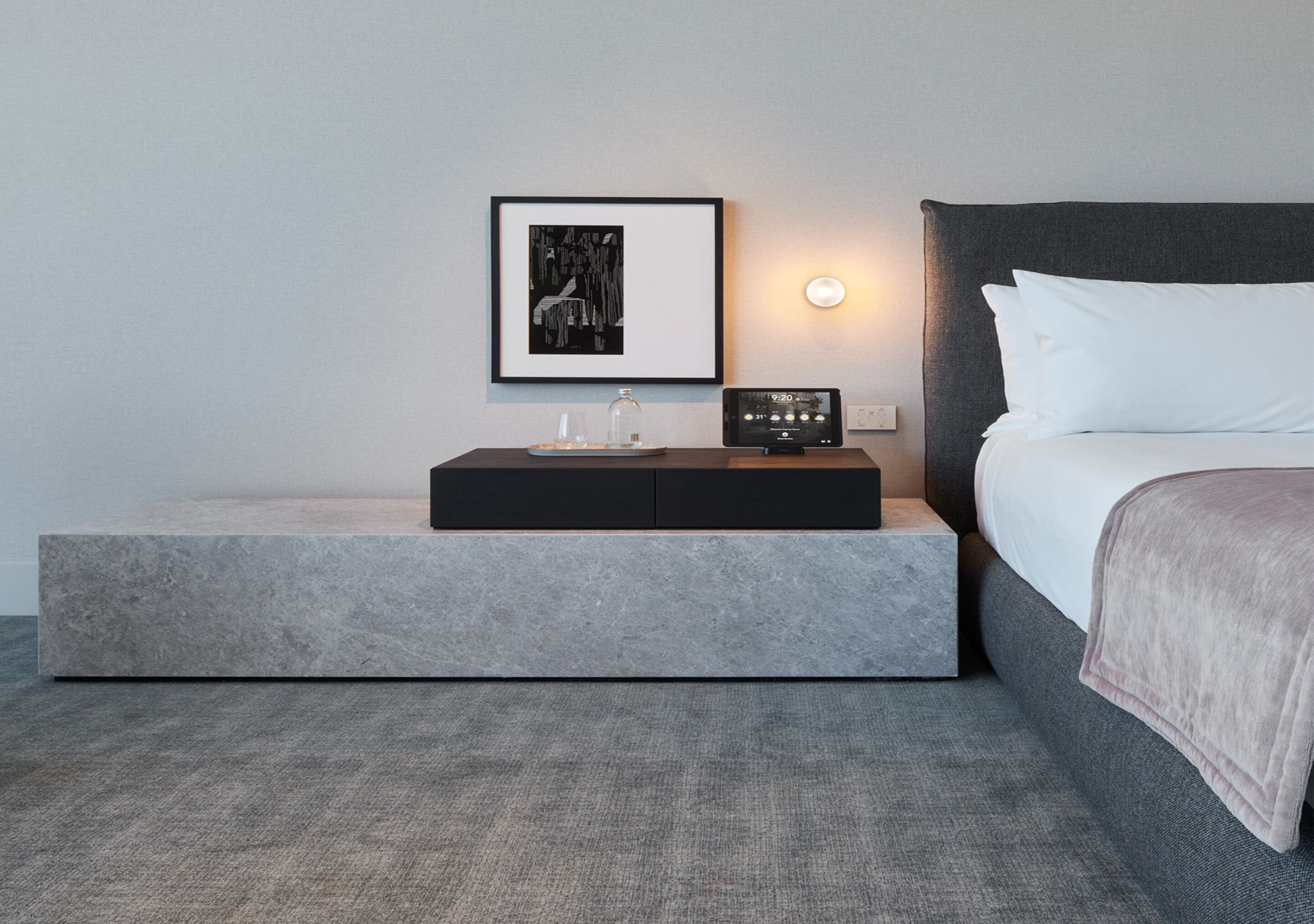 A modern bedroom with a bed, bedside table, and a wall-mounted clock.