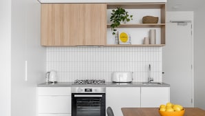 A modern kitchen with white cabinetry, a gas stove, a toaster, and a bowl of lemons on the table. - Axel Apartments 101 The Anderson (Glen Iris)
