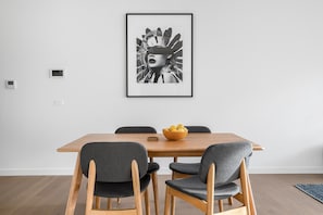 Un comedor con una mesa de madera, cuatro sillas grises tapizadas y una obra de arte blanco y negro enmarcada en la pared.