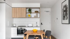 A modern kitchen with white cabinets, a gas stove, a toaster, and a bowl of lemons on the dining table. - Axel Apartments 101 The Anderson (Glen Iris)