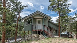 A two-story house with a porch and a deck, surrounded by pine trees. - Rocky Retreat: Relax in hot tub, 2.7 mi to RMNP, walking distance to town, #3370 (Estes Park)