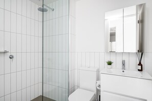 Een moderne badkamer met een douchecabine van glas, een wit toilet en een wastafel met spiegel.