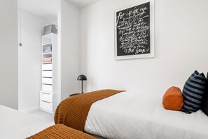 Une chambre à coucher avec un lit, des oreillers, une lampe de chevet, une armoire et un mur orné d’une citation.