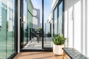 Ein moderner Balkon mit Glastür, einem Blumentopf und einer Sitzecke inklusive Tisch und Stühlen.