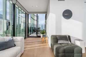 Un salon moderne avec un canapé, un fauteuil, une petite table sur laquelle est posée une plante, et une horloge murale.