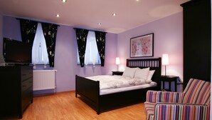 Un dormitorio con una cama, dos mesitas de noche con lámparas, un televisor, un aparador y una silla a rayas.