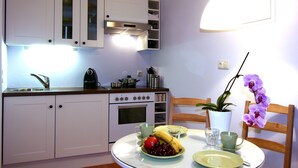 Una cocina con armarios blancos, una estufa y una mesa de comedor con un plato de fruta y una taza.