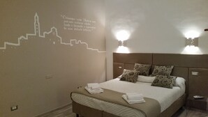 A hotel room with a bed, pillows, a headboard, wall art, and two wall-mounted lights. - DOMUS LEVI APARTMENT (Matera)